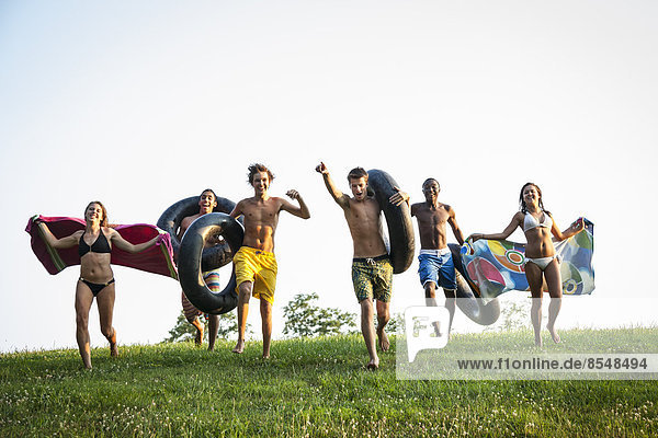 Eine Gruppe von Teenagern  Jungen und Mädchen  rannte mit Badetüchern und aufgeblasenen Schwimmern über das Gras.