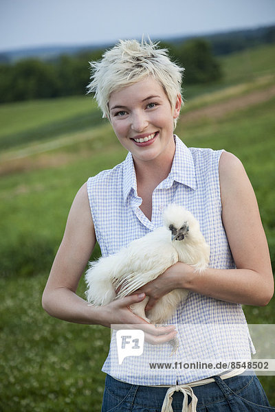 A young girl  teenager  holding a chicken with white feathers in her arms.