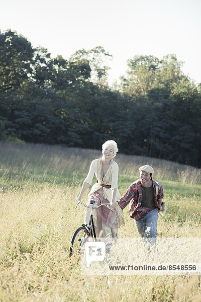 Ein Mädchen auf einem Fahrrad,  das von einem jungen Mann durch das lange Gras geschoben wird.