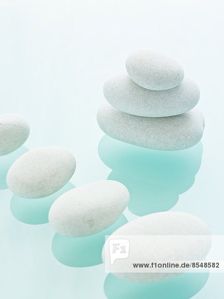 Glatte weiße Kieselsteine von einheitlicher Größe und Farbe auf einem blauen  reflektierenden Glashintergrund.