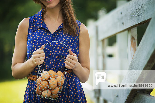 A woman holding a basket of hen's eggs gathered from the chickens on a farm.