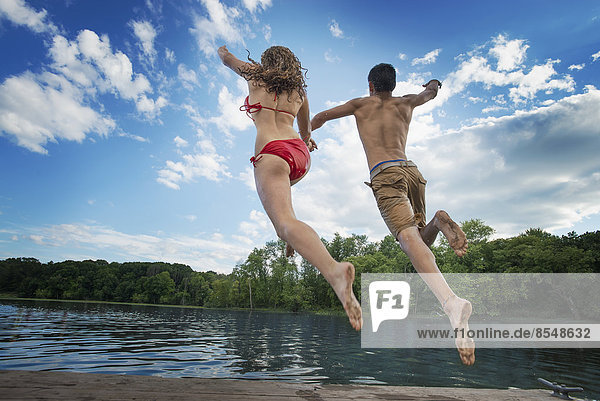 Two young people  boy and girl  running and leaping off the jetty into a lake or river.