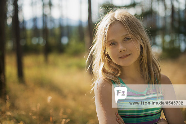 A child with long blonde hair in woodland by a lake.