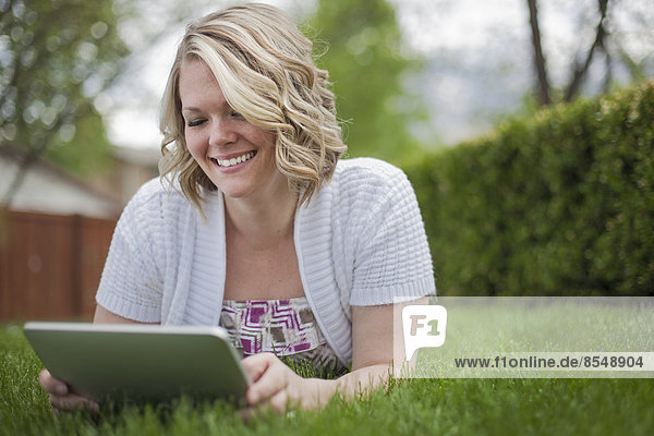 A young woman reading using a handheld electronic device  or e reader.