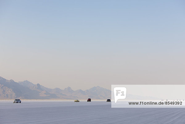 Cars driving on Bonneville Salt Flats during Speed Week. Dusk.
