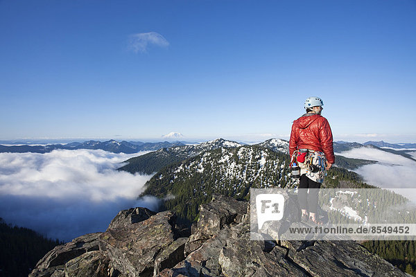 Ein Felskletterer steht auf dem Gipfel eines Gipfels  nachdem er mit Hilfe eines Seils und eines Schutzes auf den Gipfel geklettert ist.