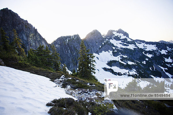 Ein junger Mann wandert um ein Schneefeld herum  während er sich auf den Gipfel eines großen Berges in den Cascades of Washington  USA  begibt.