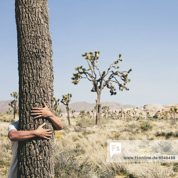 Man hugging a Joshua Tree in Joshua Tree national park.