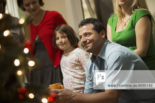 Eine weihnachtliche Versammlung  Erwachsene und Kinder in einem Raum um einen Weihnachtsbaum  die gemeinsam feiern.