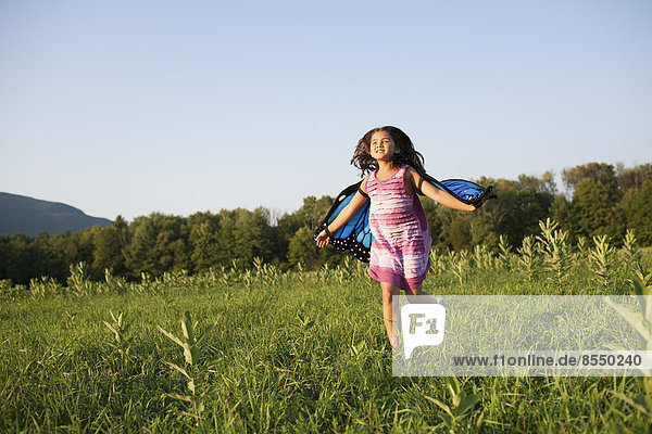 A young girl running across a field  wearing fabric butterfly wings.