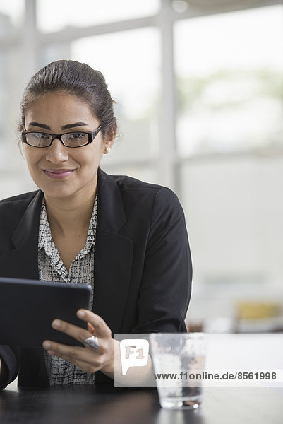 Junge Berufstätige bei der Arbeit. Eine Frau in einer schwarzen Jacke  die ein schwarzes digitales Tablett benutzt.