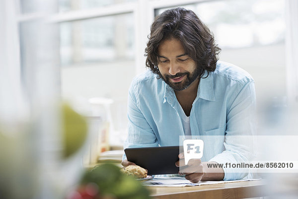 Eine Büro- oder Wohnungseinrichtung in New York City. Ein bärtiger Mann in einem türkisfarbenen Hemd mit einem digitalen Tablet.