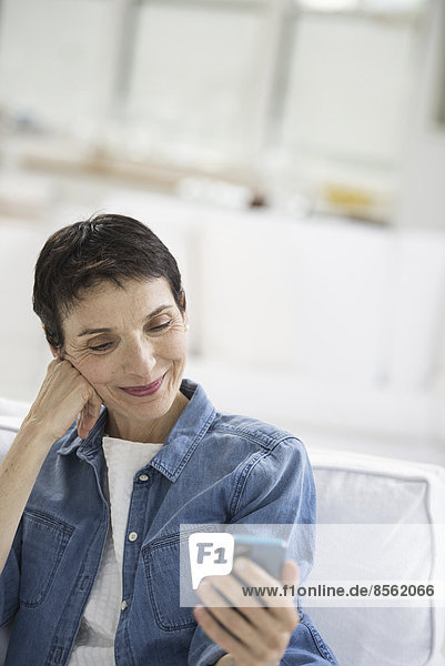 Ein Großraumbüro in New York City. Eine reife Frau mit grauen Haaren  die ein Jeanshemd trägt und auf den Bildschirm eines Smartphones schaut.
