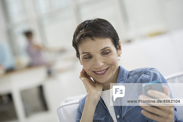 Professionals in the office. A light and airy place of work. A mature woman in a blue denim shirt looking at a blue smart phone.