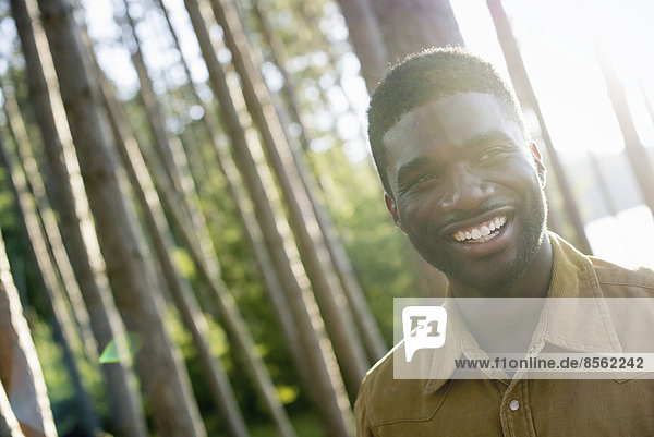 Ein Mann  der im Sommer unter dem Schatten der Bäume in die Kamera lächelt.