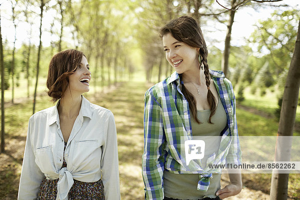 Zwei junge Frauen gehen eine Baumallee entlang.