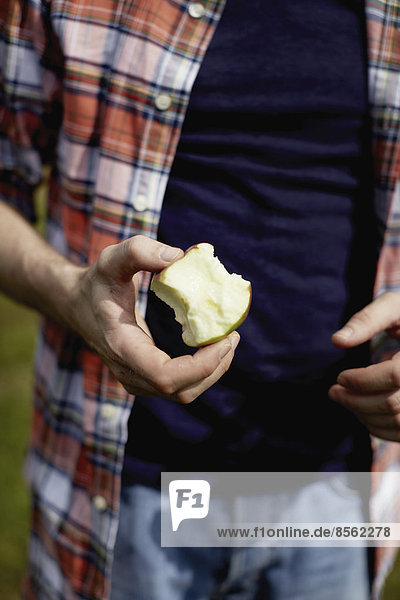 Mittelteil eines Mannes  der ein kariertes Hemd trägt und einen halb gegessenen Apfel hält.