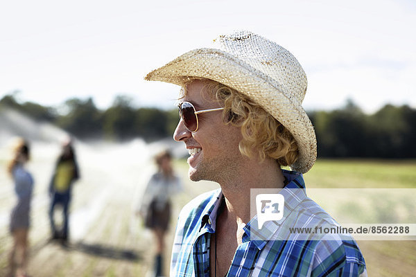 A young man in straw hat and sunglasses. Irrigation sprinklers in the field.