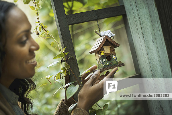 Scenes from urban life in New York City. A woman holding a small painted bird house in an enclosure.