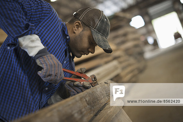 Ein Mann arbeitet auf einem ehemaligen Holzlager. Er benutzt ein Werkzeug  um Metalle aus einem Stück Altholz zu entfernen. Werkstatt.