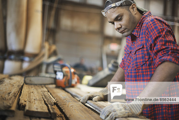 Eine zurückgewonnene Holzwerkstatt. Ein Mann misst und kontrolliert Bretter aus Holz für die Wiederverwendung und das Recycling.