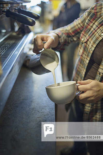 A person  barista  making coffee  and pouring frothed milk from a jug into a cup for a cappuccino. Coffee shop.