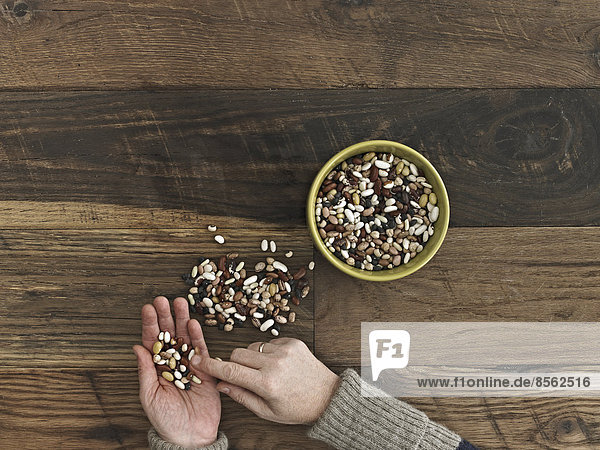 Eine Person sortiert verschiedene Arten von Bohnen und Hülsenfrüchten in ihren Händen auf einer hölzernen Tischplatte.