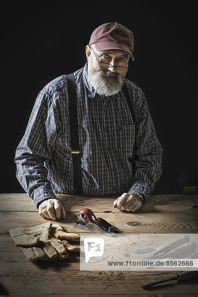 Ein Mann,  der in einer wiederaufgearbeiteten Holzlagerhalle arbeitet. Er hält Werkzeuge und arbeitet an einem verknoteten und unebenen Stück Holz.
