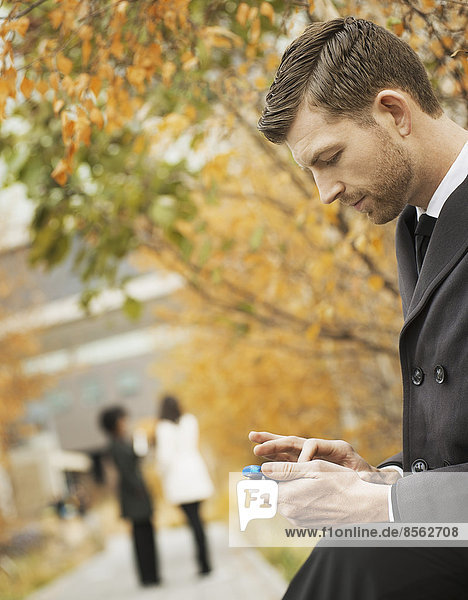 Stadtleben. Ein Mann im Park kontrolliert und schreibt SMS  hält Kontakt  benutzt ein Mobiltelefon.