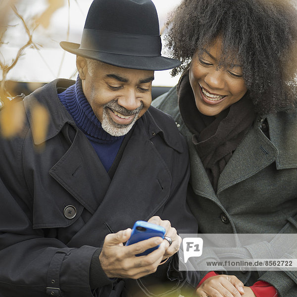 City life. Two people  a man and woman standing side by side  keeping in contact  using mobile phones  and checking the screen  laughing.