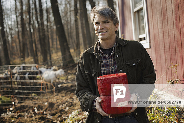 Ein Mann steht auf einem Bauernhof und hält zwei Blöcke Ziegenkäse in der Hand.