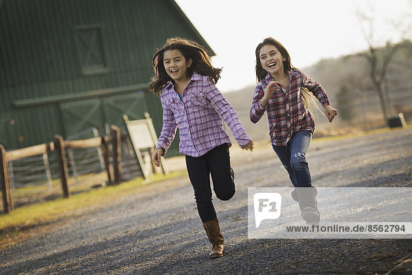 Zwei Kinder laufen an einer Straße entlang  an einem Bauernhofgebäude vorbei  auf einem Biohof.