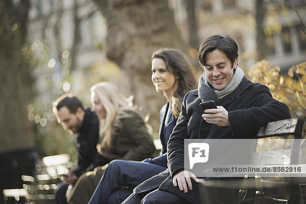 Group on bench in urban park using smartphones