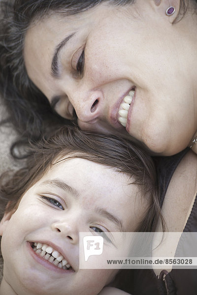 Die Nahaufnahme einer Mutter und einer Tochter  die lächelnd und lachend mit dem Kopf zusammen liegen.