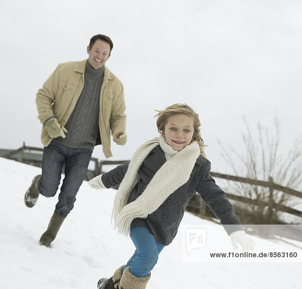 A man chasing a young girl in the snow. Farm in winter.