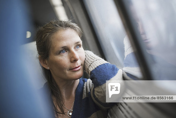 A woman sitting at a window seat in a train carriage  resting her head on her hand. Looking into the distance.