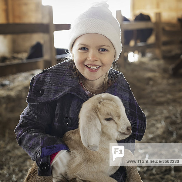 Ein Kind im Tierstall  das ein Ziegenbaby hält und streichelt.
