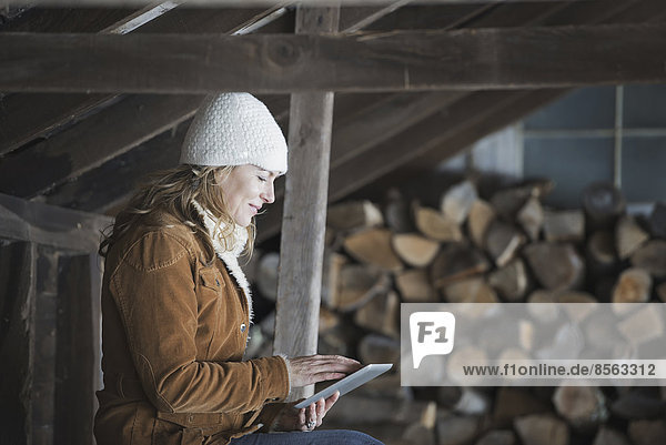 An organic farm in upstate New York  in winter. A woman sitting in an outbuilding using a digital tablet.