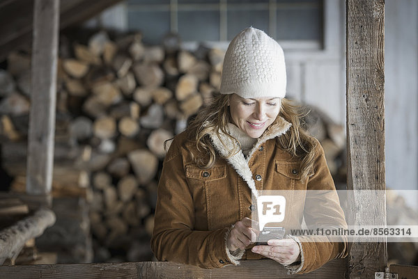 An organic farm in upstate New York  in winter. A woman in sheepskin coat and woollen hat using a cell phone.