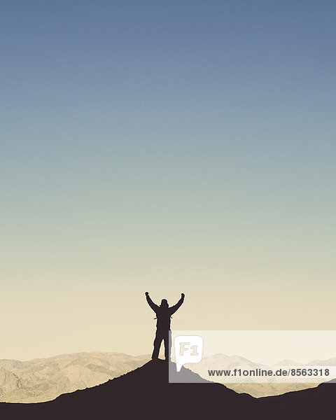 Silhouette of a male hiker wearing a backpack and standing on a hilltop in Death Valley national park.