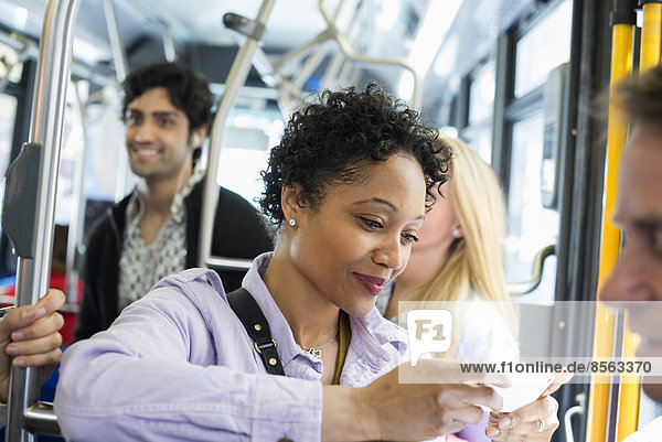 New Yorker Stadtpark. Menschen  Männer und Frauen in einem Stadtbus. Öffentliche Verkehrsmittel. In Kontakt bleiben. Eine junge Frau  die ihr Mobiltelefon überprüft oder benutzt.
