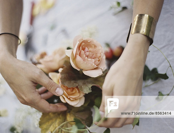 Eine Frau arrangiert frische Blumen auf einer mit einem weißen Tuch bedeckten Tischplatte. Pfirsichfarbene Rosen.