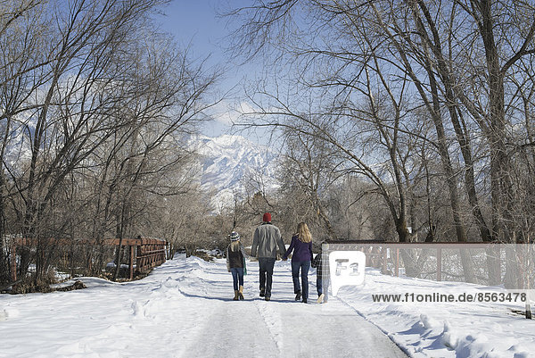 Winterlandschaft mit Schnee auf dem Boden. Eine Familie  Erwachsene und zwei Kinder  die eine leere Straße entlanglaufen.