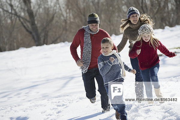 Winter scenery with snow on the ground. Family walk. Two adults chasing two children.