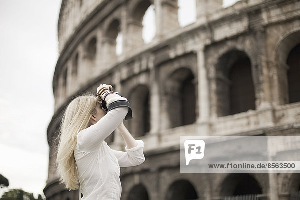 Eine Frau vor dem Amphitheater des Kolosseums in Rom beim Fotografieren.