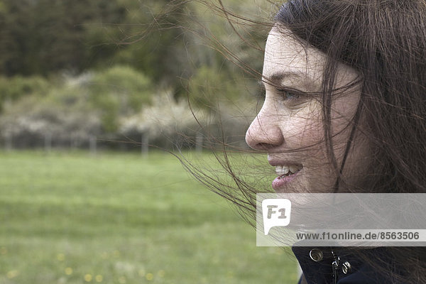 Eine junge Frau im Profil. Ihr braunes Haar weht über ihr Gesicht. Im Freien. Im Frühling.