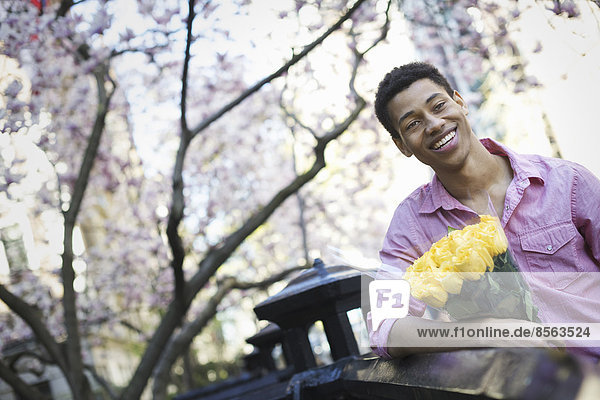 Stadtleben. Ein junger Mann im Frühling im Park mit einem Strauß gelber Rosen in der Hand.