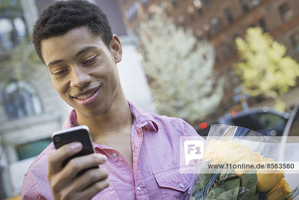 Urbaner Lebensstil. Ein junger Mann mit kurzen schwarzen Haaren  der ein rosa Freizeithemd trägt. Er hält ein Smartphone in der Hand.