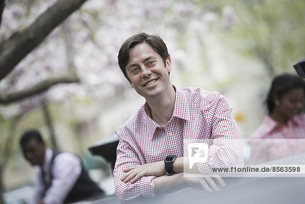 City life in spring. A man sitting outdoors in a city park. Looking at the camera and smiling.