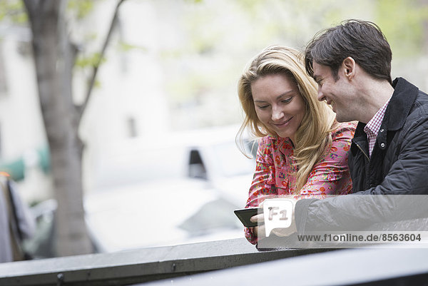 Stadtleben im Frühling. Jugendliche im Freien in einem Stadtpark. Zwei Menschen sitzen nebeneinander und schauen auf ein Smartphone.